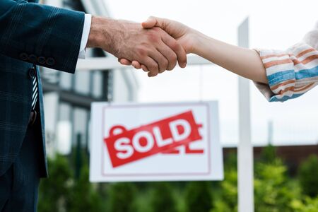 Selective focus of broker and woman shaking hands near board with sold letters