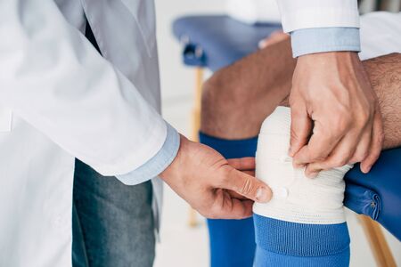 Partial view of Physiotherapist in white coat putting elastic bandage on leg of football playerの写真素材