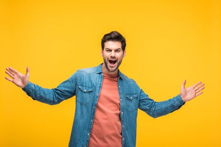 Handsome excited man gesturing with open palms isolated on yellow background