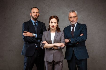 Attractive businesswoman and handsome businessmen standing with crossed arms on grey backgroundの写真素材
