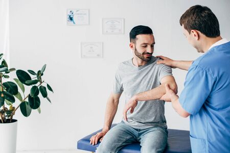 Selective focus of chiropractor examining patient shoulder in massage cabinet at clinicの写真素材