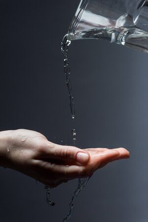 Cropped view of woman with jug and flowing water on dark backgroundの写真素材