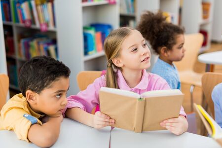 Selective focus of cute kid holding book near African American childrenの写真素材
