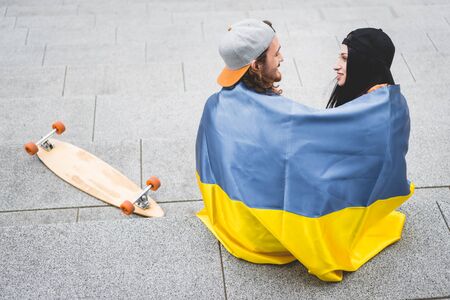 High angle view of couple with Ukrainian flag sitting on stairs near skateboard, looking at each otherの写真素材