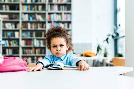 Bored African American kid sitting near book in libraryの写真素材
