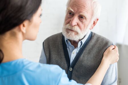 Selective focus of nurse putting hands on serious and grey haired manの写真素材
