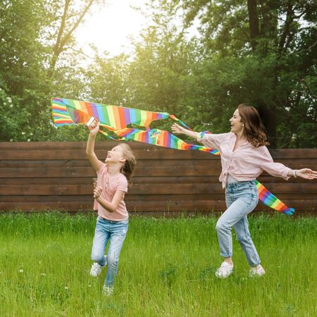 Happy mother with outstretched hands near cute kid with colorful kiteの写真素材