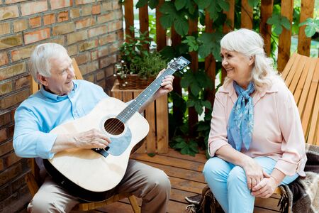 Happy retired woman looking at husband playing acoustic guitarの写真素材