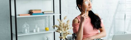 Panoramic shot of attractive Asian woman in glasses sitting in officeの写真素材