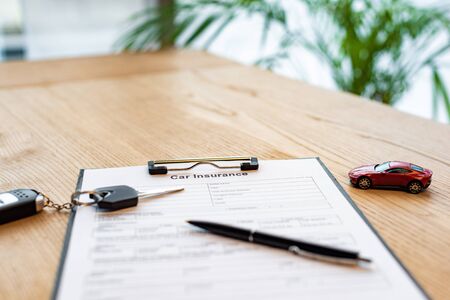Selective focus of car key and pen on clipboard with document near toy car