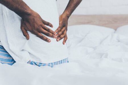 Cropped view of African American man suffering from back pain in bedroomの写真素材