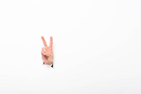 Man showing peace sign from hole in paper wall on white background with copy spaceの写真素材