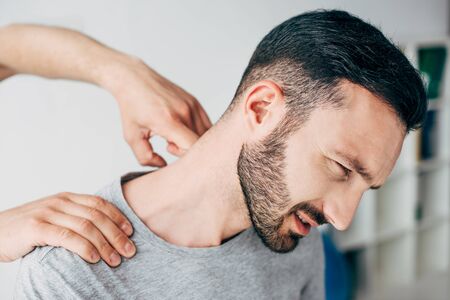 Chiropractor massaging neck of bearded man in hospital