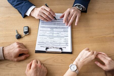 Cropped view of car dealer signing document near customers on office