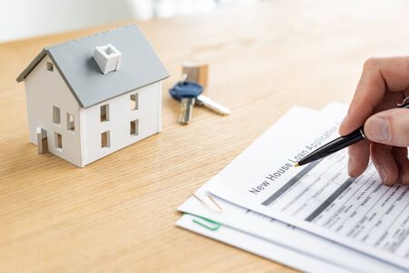 Cropped view of house dealer holding pen near document with new house loan lettering, house model and keysの写真素材
