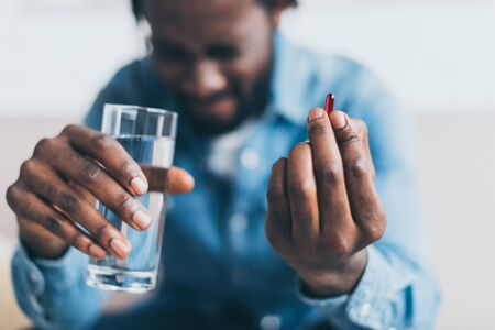 Selective focus of African American man suffering from hurt and holding glass of water and pillの写真素材