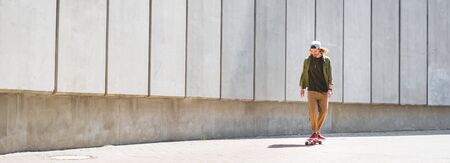 Panoramic view of handsome man riding on skateboard near concrete wallの写真素材