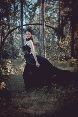 Side view of brunette woman in witch costume standing on forest background, looking awayの写真素材