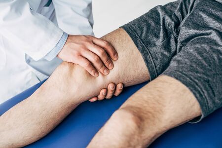 Partial view of Physiotherapist massaging leg of man on massage table in hospitalの写真素材