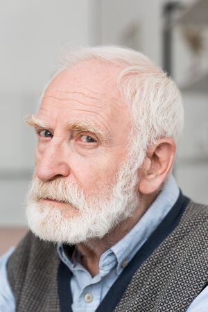 Sad and bearded grey haired man looking at camera