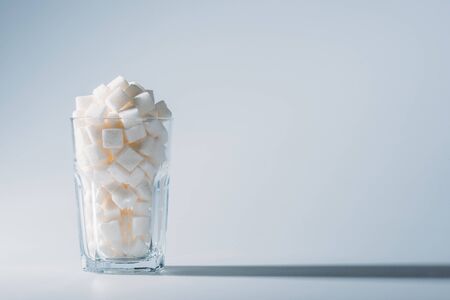 Glass full of white refined sugar cubes on grey background with copy spaceの写真素材