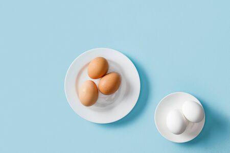 Top view of fresh brown and white eggs on white plates on blue backgroundの写真素材