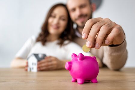 Selective focus of man putting coin in pink piggy bank and cheerful womanの写真素材
