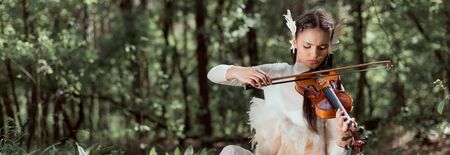 Panoramic view of brunette woman in white swan costume playing on violinの写真素材