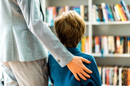 Back view of kid standing with woman in libraryの写真素材