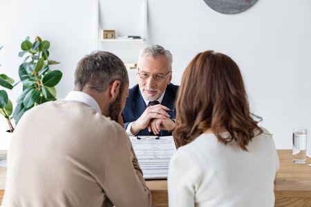 Back view of man and woman sitting near bearded car dealer and clipboard with agreementの写真素材