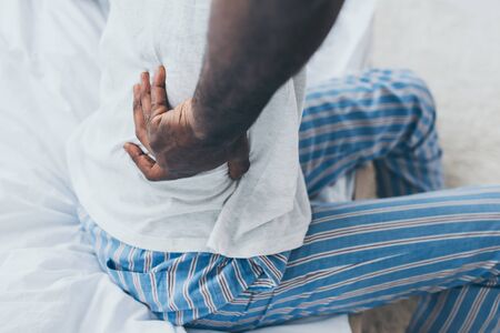Cropped view of African American man suffering from back pain in bedroomの写真素材