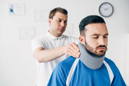Chiropractor examining good-looking football player in neck brace in hospitalの写真素材