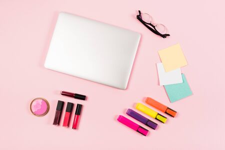 Top view of laptop, glasses, highlighters and decorative cosmetics on pink backgroundの写真素材
