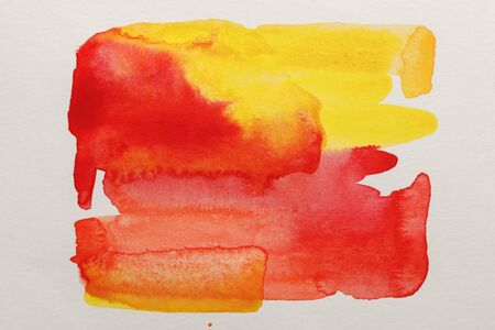 Top view of yellow and red watercolor paint spills on white paper backgroundの写真素材