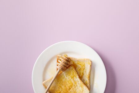 Top view of toasts with honey and wooden dipper on white plate on violet backgroundの写真素材