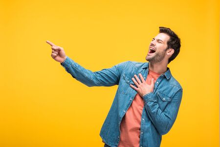 Good-looking man laughing and pointing with finger isolated on yellow backgroundの写真素材