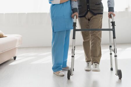 Cropped view of nurse walking with senior man in bright room