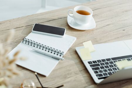 Selective focus of laptop near smartphone with blank screen, cup of tea and notebookの写真素材