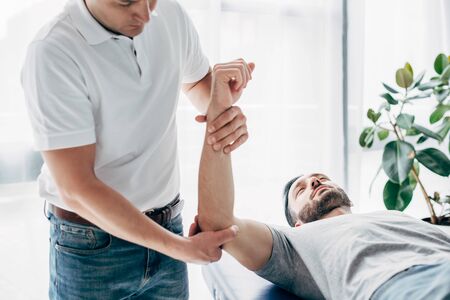Physiotherapist stretching arm of bearded patient in hospitalの写真素材