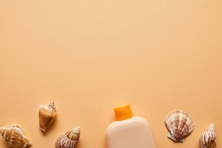 Top view of sunscreen lotion in bottle near seashells on beige background