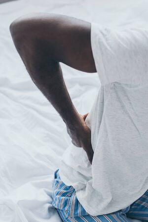 Cropped view of African American man suffering from back pain in bedroomの写真素材