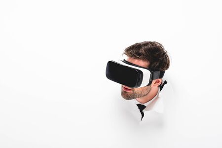 Bearded man in Virtual reality headset behind hole in wall on white background with copy spaceの写真素材