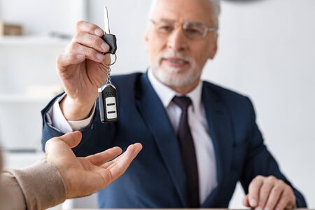 Selective focus of car dealer giving car key to man in officeの写真素材
