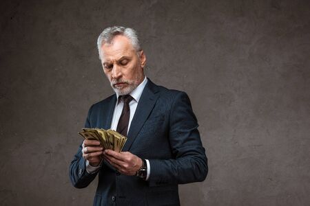 Businessman in suit holding dollar banknotes in hands on grey background