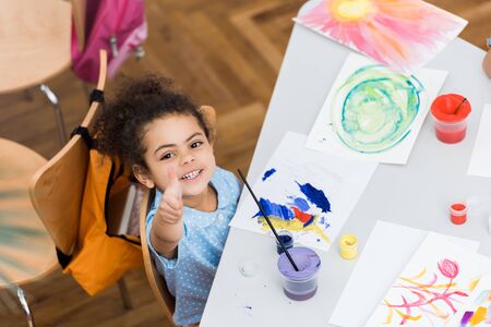 Overhead view of happy African American kid pointing with finger near paper with paintingの写真素材