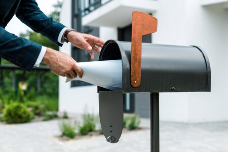 Cropped view of man putting blank paper in mail box near houseの写真素材