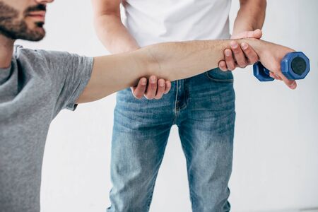 Cropped view of chiropractor stretching arm of patient with dumbbell on grey backgroundの写真素材