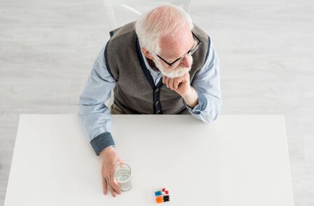 Overhead view of pensive man looking away, sitting behind table with pills and water in glassの写真素材