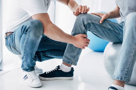 Cropped view of Physiotherapist massaging leg of patient sitting on fitness ball in hospitalの写真素材