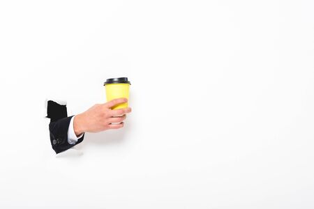 Partial view of man holding coffee to go from hole in wall on white background with copy spaceの写真素材